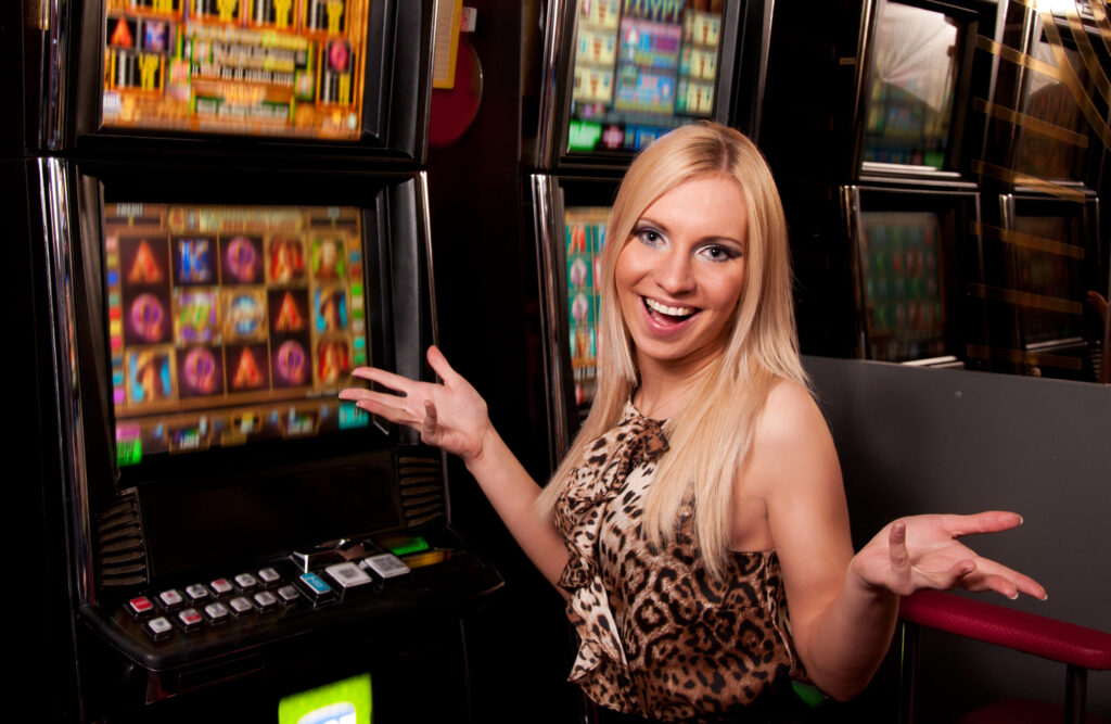 En ung kvinde viser med sit glade ansigt og indbydende kropssprog sin glæde ved at blive underholdt af spillemaskiner på et rigtigt casino med penge på højkant.